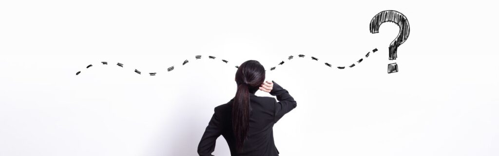 A woman in a suit looking at a drawing on a white wall of a squiggly dotted line connecting to a question mark.