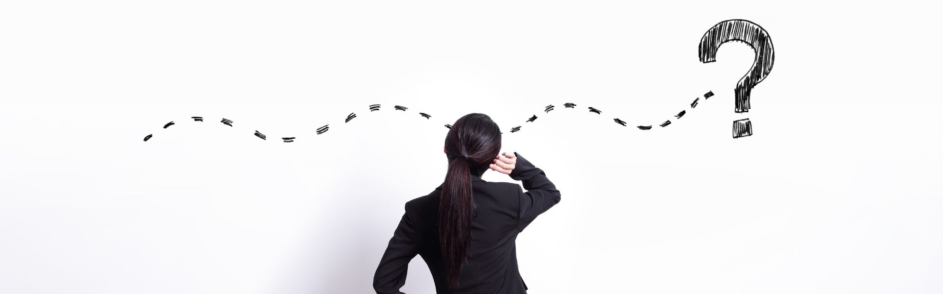 A woman in a suit looking at a drawing on a white wall of a squiggly dotted line connecting to a question mark.