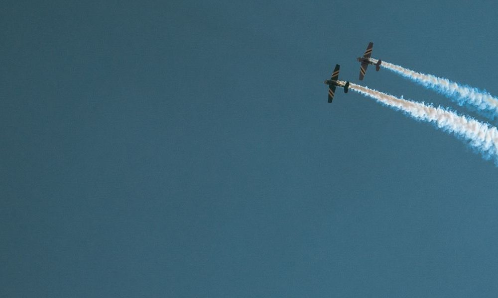 Two airplanes with tails on contrails in the sky.