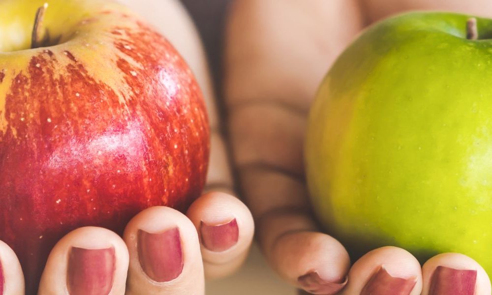A person holding a red apple in one hand and a green apple in the other hand.