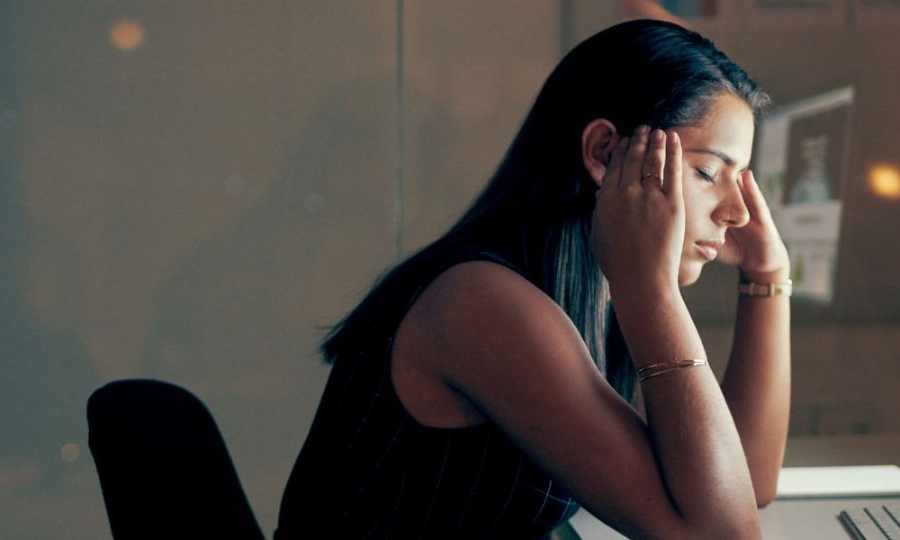 A woman sitting in front of a computer with her head in her hands.
