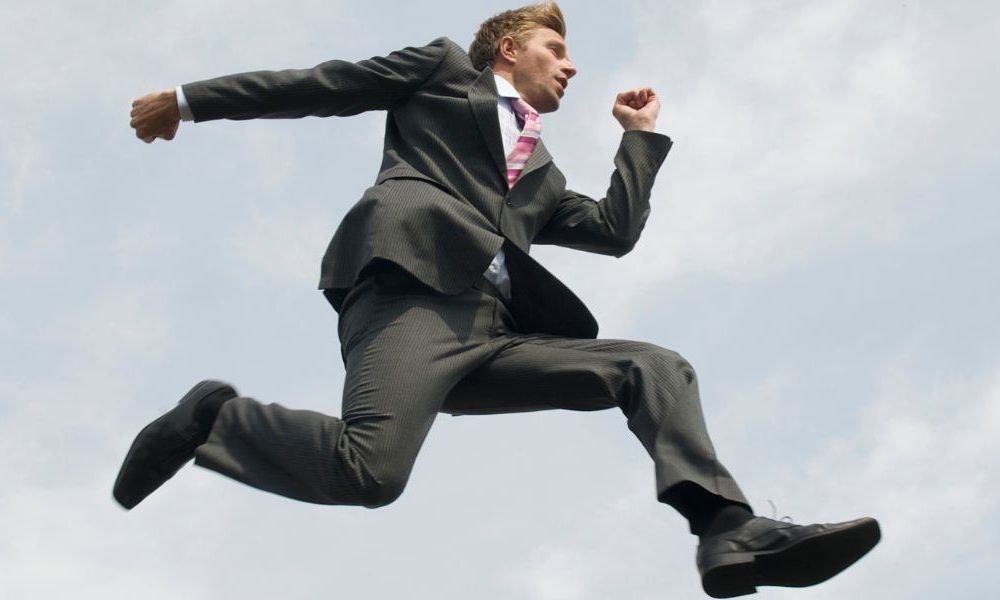 A man in a suit jumping between rock ledges.