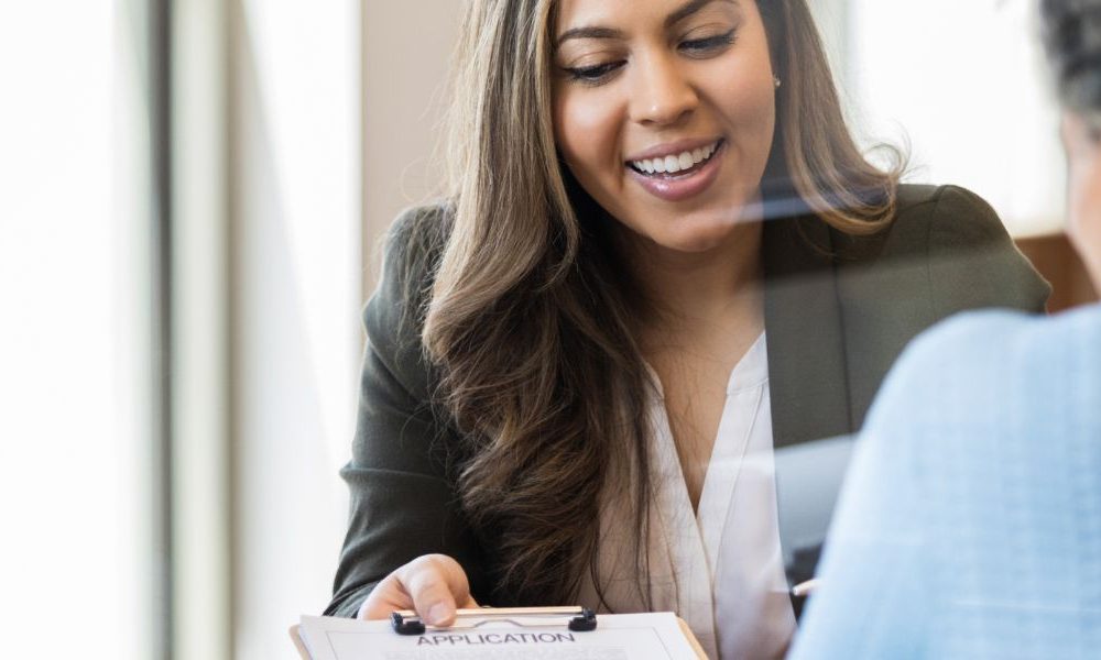A banker handing an application on a clipboard over to a client.