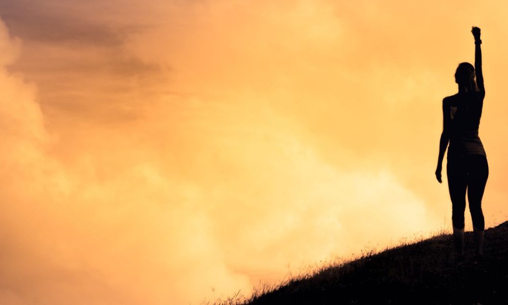 A person standing on a hill with their fists raised in the air.