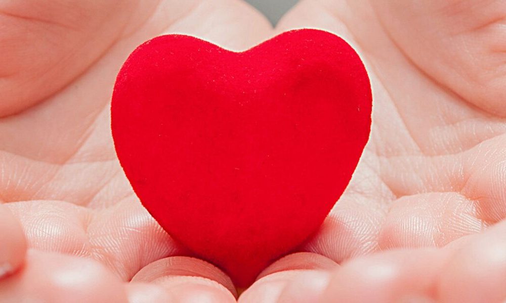Two hands holding a red heart.