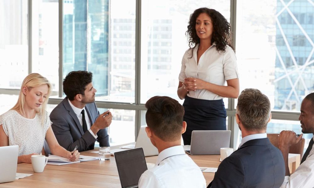 An image of a woman giving a presentation to a group of employees in an office board room.