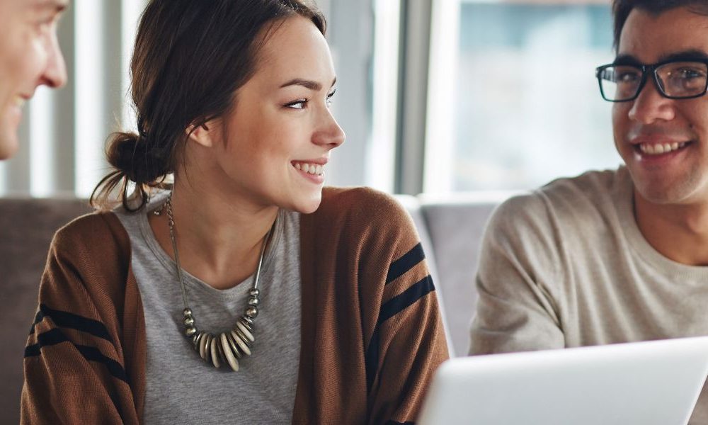 Three people sitting together at a cafe in front of an open laptop.
