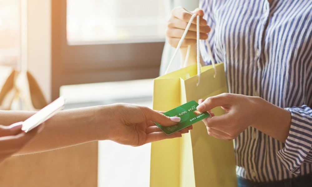 A person holding a shopping bag and handing a business owner a card.