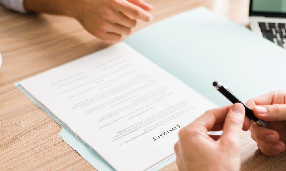 A banker holding a pen with a contract on a table in front of clients.